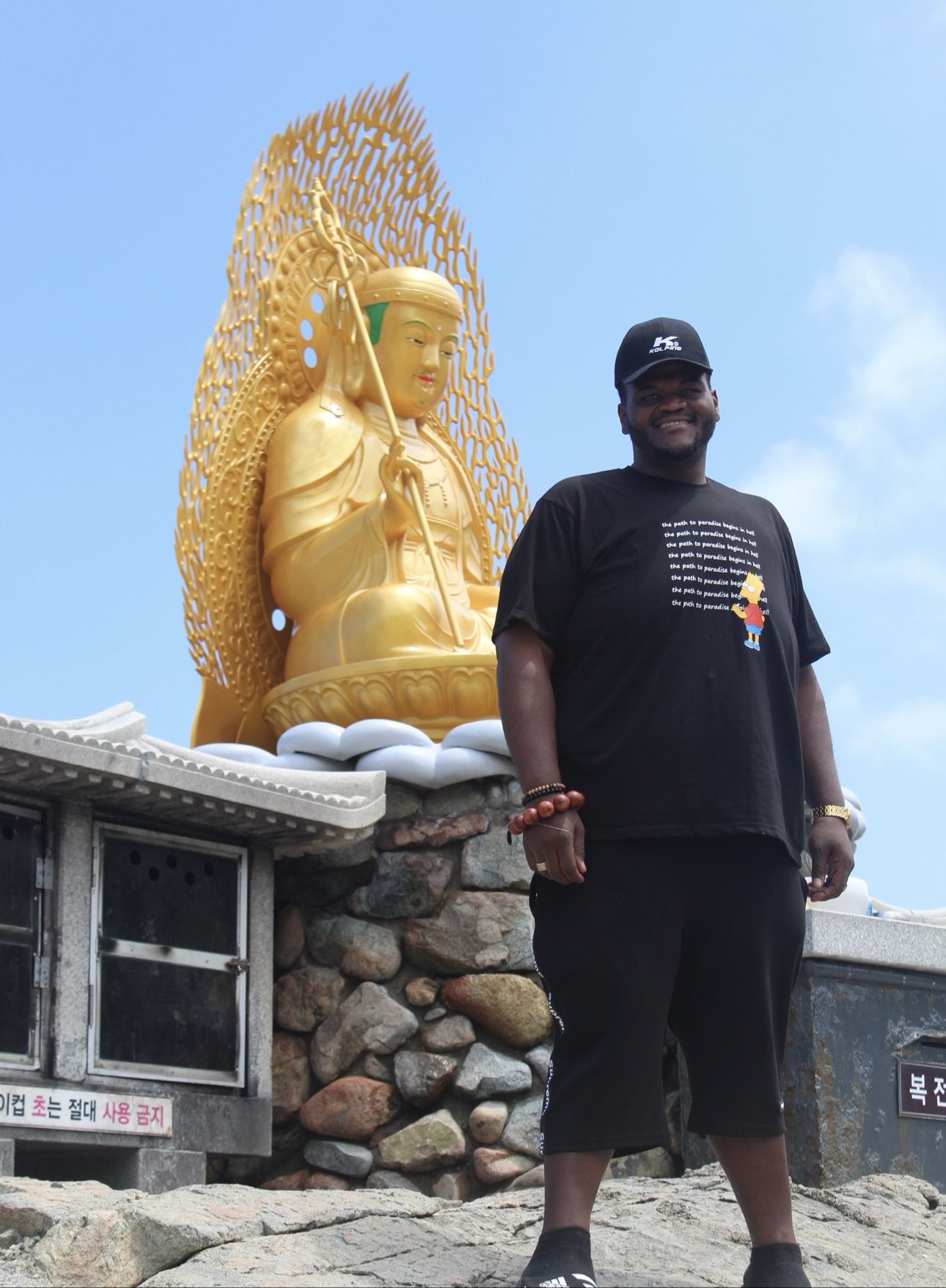 A traveler standing beside a monumental golden Buddha beneath a clear blue sky in Busan