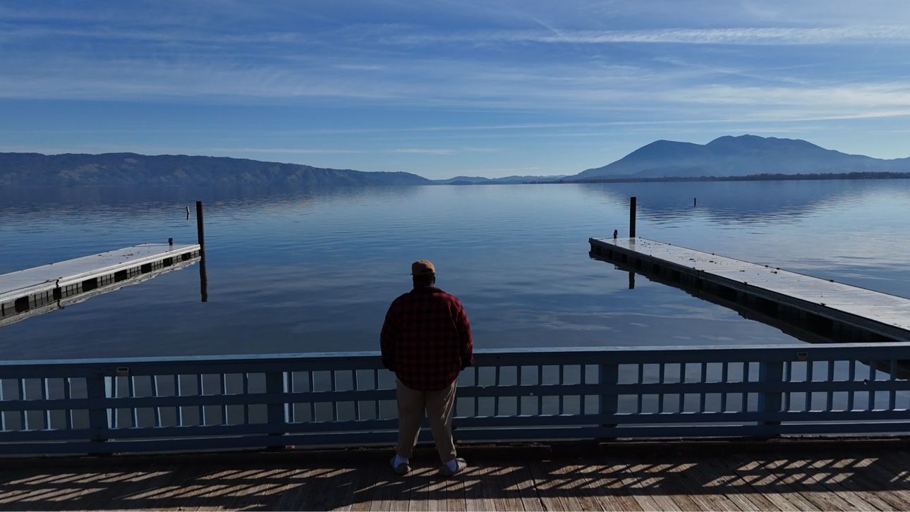 A traveler stands between two snow-dusted docks overlooking a still mountain lake