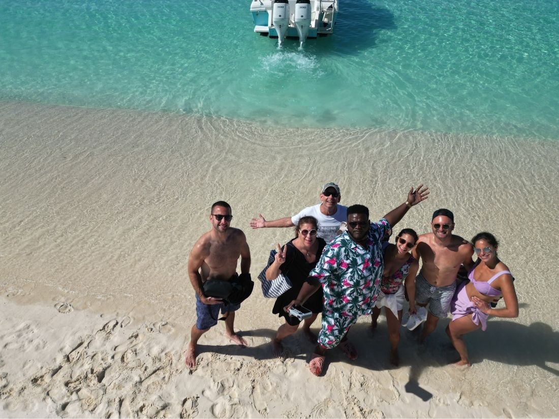 Aerial view of a group waving from a white sandbar, boat anchored behind